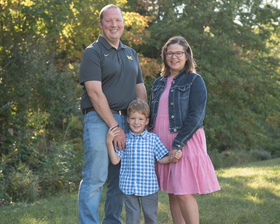 Family of three standing in a grassy area with trees in the background