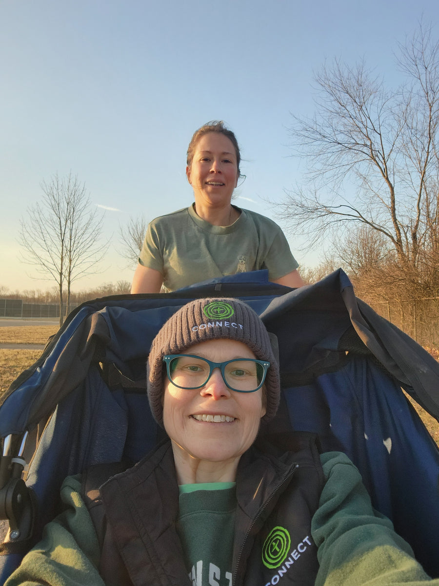 A woman pushing her sister through a beautiful park with a jogging stroller.