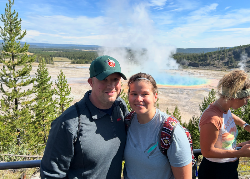 Two people posing for a photo with a geothermal area in the background