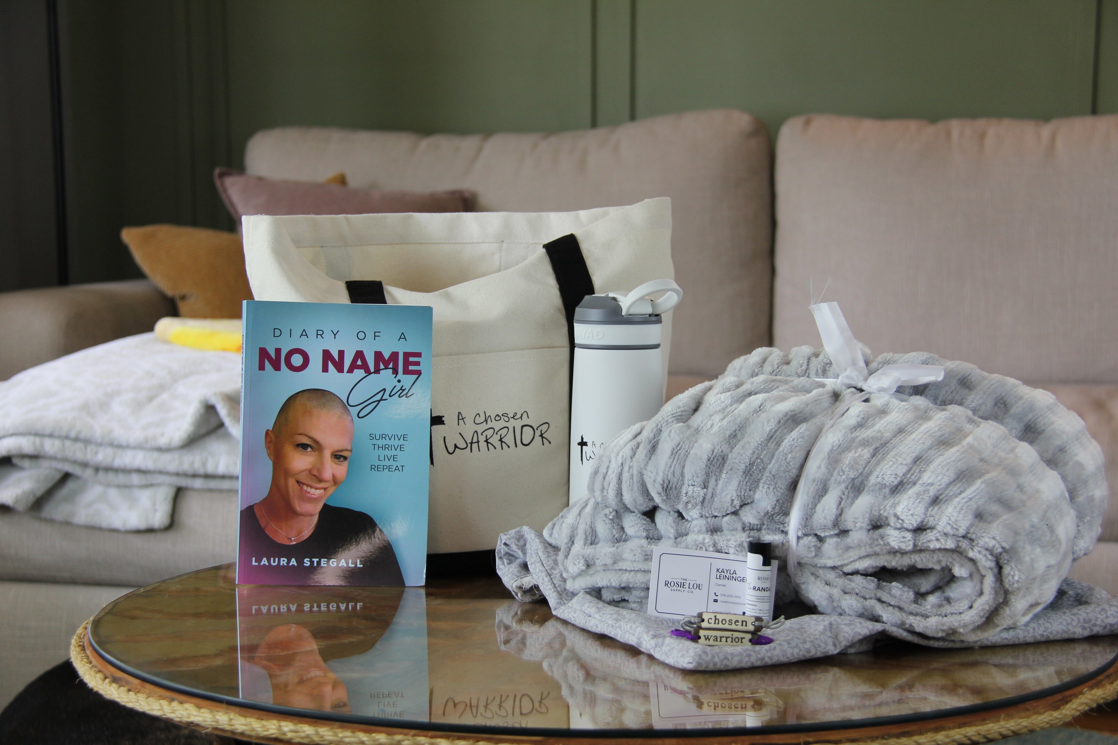 Book titled 'Diary of a No Name Girl' on a coffee table with folded blankets and a tumbler.