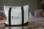 White tote bag with black straps and 'A Chosen Warrior' text on a glass table.