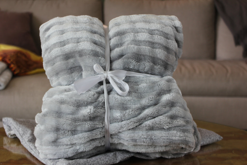 A soft fuzzy blanket tied with a white ribbon on a wooden surface with a blurred sofa in the background.