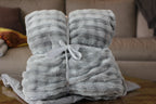 A soft fuzzy blanket tied with a white ribbon on a wooden surface with a blurred sofa in the background.